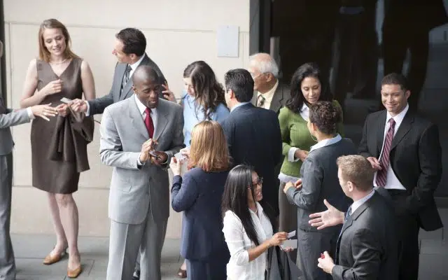 A diverse group of business professionals networking outdoors, exchanging cards and conversations, representing the importance of communicating authenticity in professional relationships.