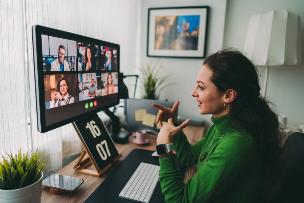 Professional woman in a green sweater discussing a B2B tech PR strategy during a virtual team meeting on a desktop computer.
