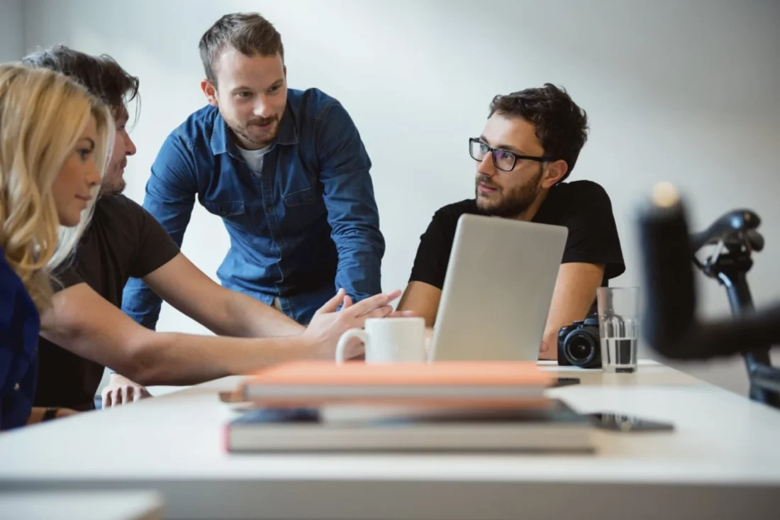 Group of colleagues collaborating around a laptop during a meeting, discussing press release strategy for B2B tech.