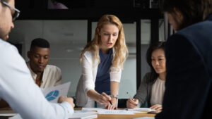 Woman leading a meeting with diverse members of a B2B tech PR firm, reviewing charts and graphs on a table.