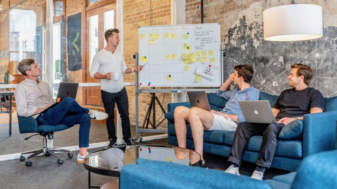 A team of professionals in a modern office discusses strategy in front of a whiteboard with sticky notes, symbolizing the process of hiring a PR agency for B2B tech thought leadership.
