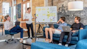 A team of professionals in a modern office discusses strategy in front of a whiteboard with sticky notes, symbolizing the process of hiring a PR agency for B2B tech thought leadership.