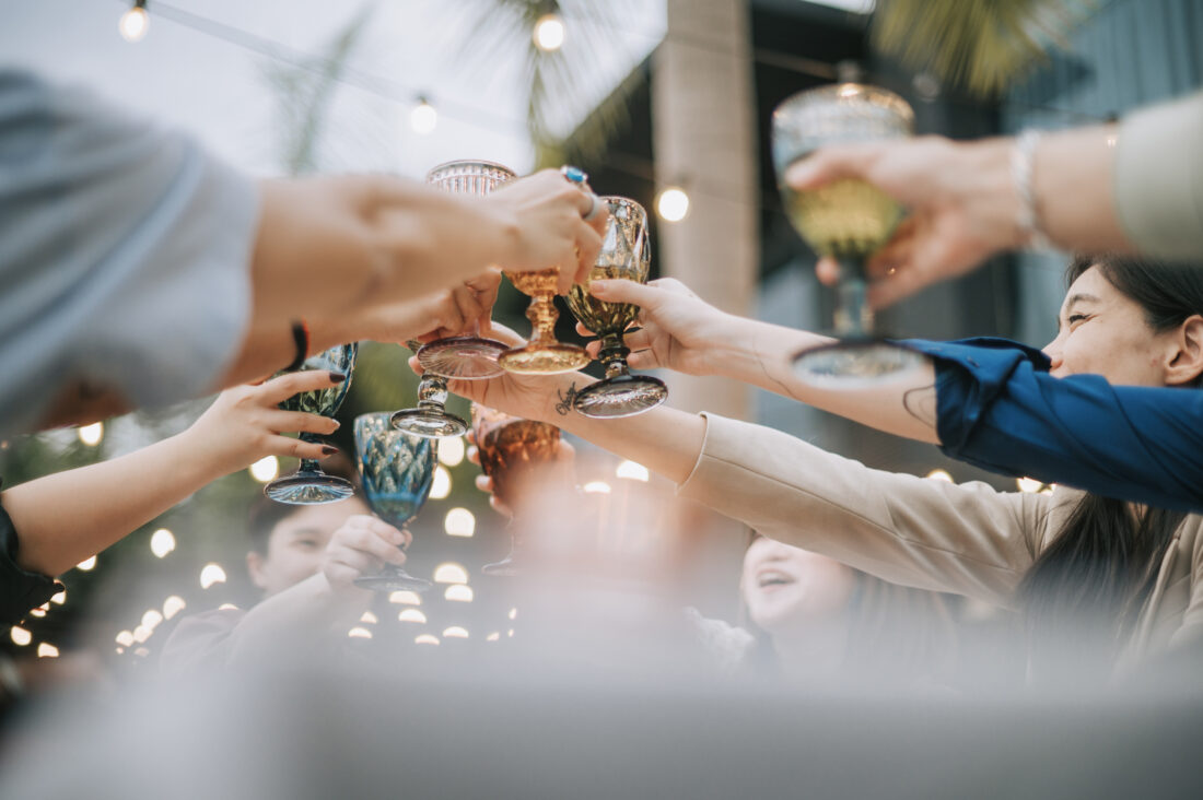 A celebratory toast with colorful glasses raised by a group of smiling colleagues, symbolizing the GMG leadership transition.