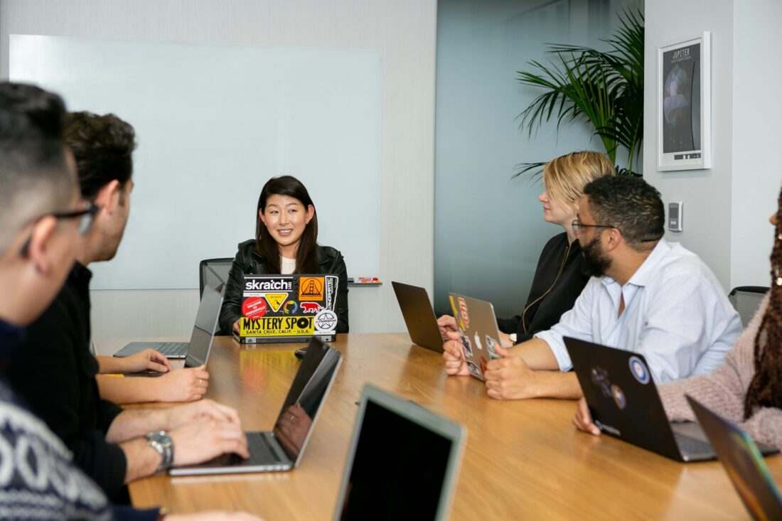 A diverse group of professionals in a conference room meeting with laptops open, discussing strategy and collaboration, representing how PR influences analyst reports through consistent communication and visibility.