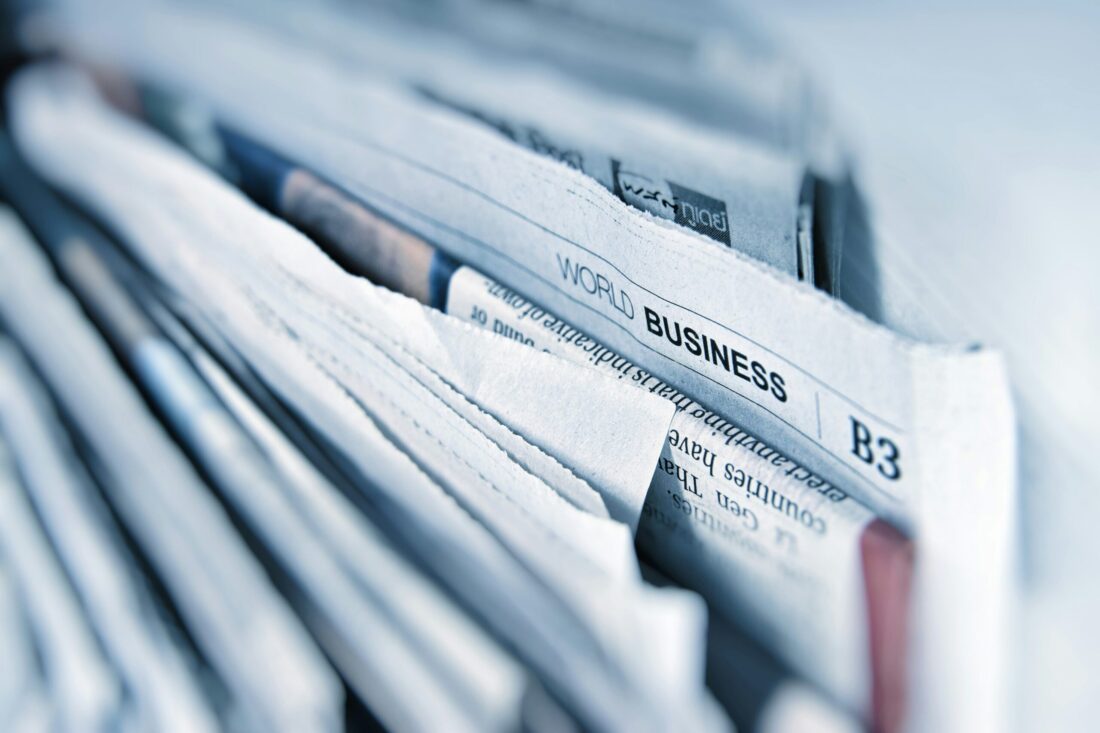 A close-up stack of business newspapers highlighting industry journalism, representing how to get cited by AI through trade coverage.