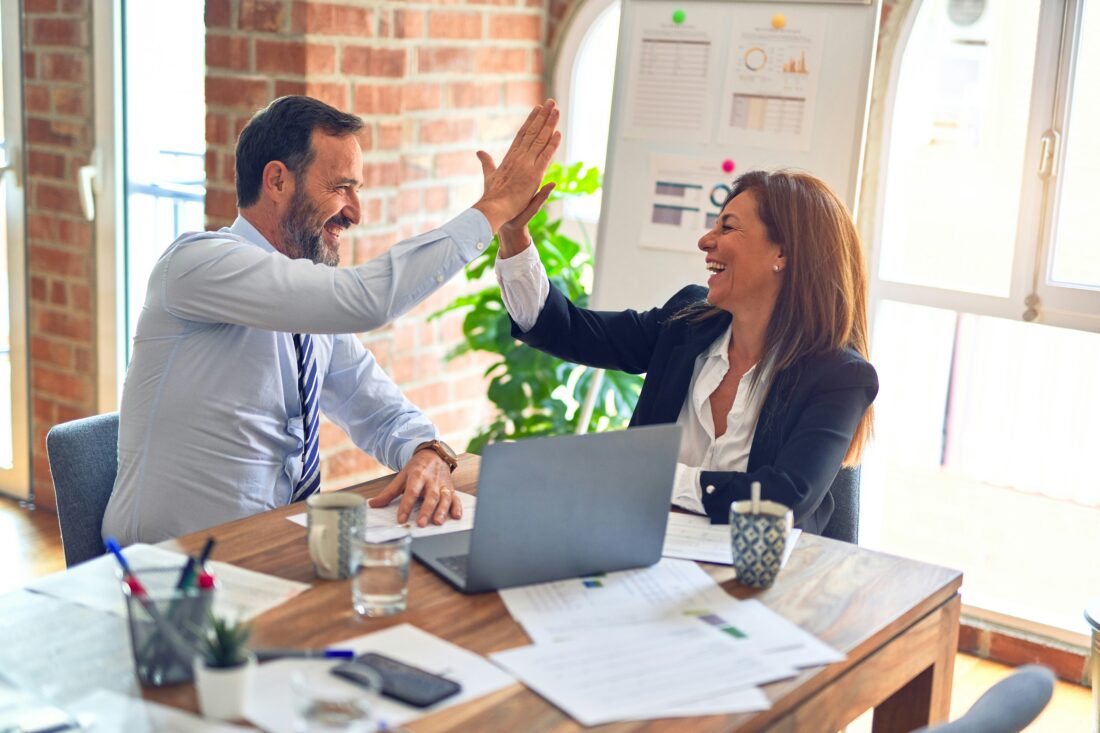 Two business professionals in a modern office celebrate success with a high-five, symbolizing teamwork and achievement—an image representing how to use case studies in B2B tech PR to build credibility and growth.