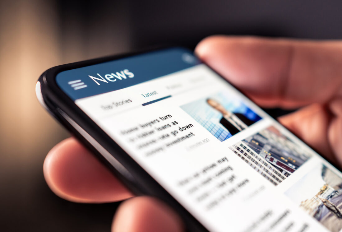 Person scrolling through a digital news feed on a smartphone screen, reading an article about how to get B2B tech stories in top-tier media.