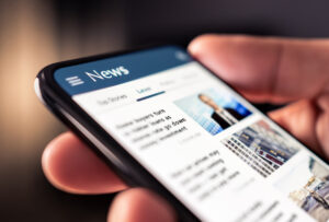 Person scrolling through a digital news feed on a smartphone screen, reading an article about how to get B2B tech stories in top-tier media.