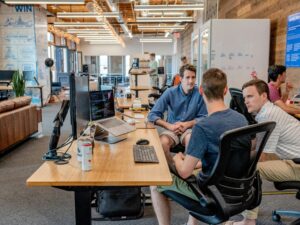 A group of colleagues in a modern open office discuss strategy around a laptop, representing collaboration on how to measure PR in a zero-click world.