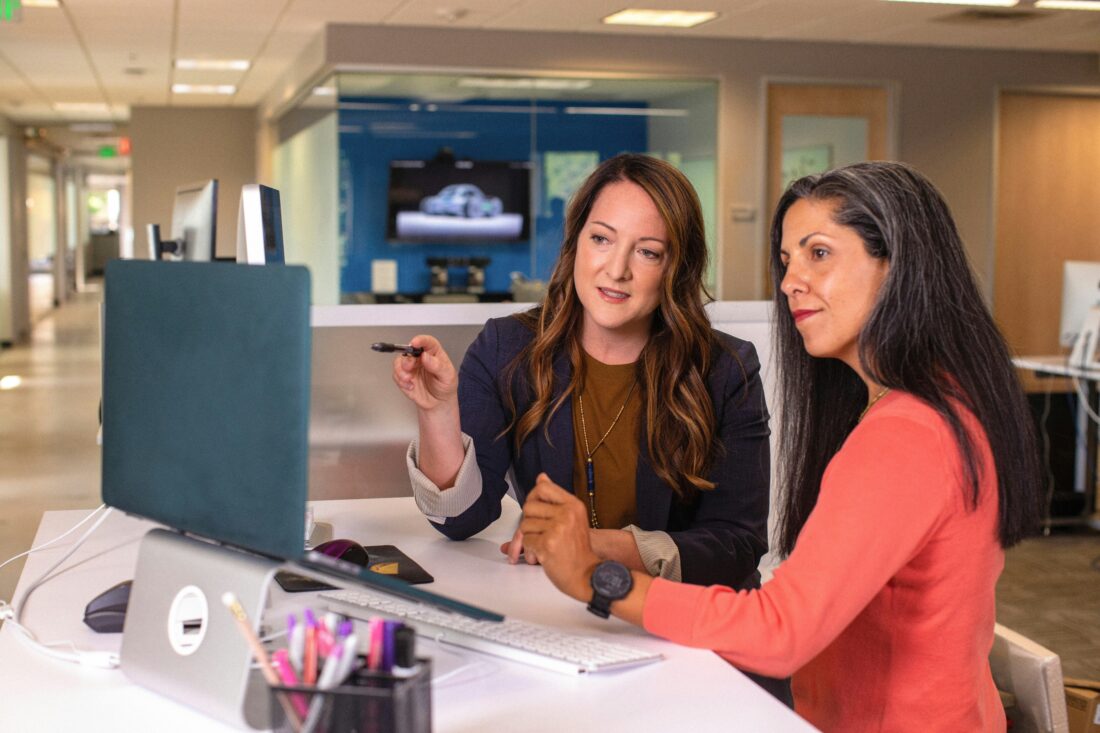 Two professionals discussing a PR agency investment strategy while reviewing data on a computer in a modern office setting.
