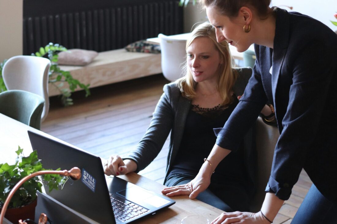 Two professional women reviewing a roadmap for engaging a B2B tech PR agency on a laptop in a modern office setting.