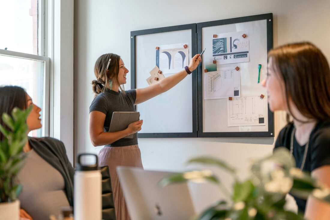 A person points to a wall of design plans while teammates look on during a strategy session about AI visibility and user intent.