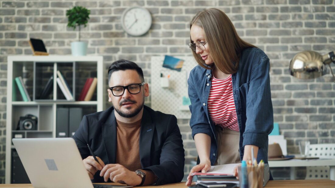 Two business leaders reviewing content together at a desk, illustrating how authority-building press releases shape executive perspective and AI-era brand credibility.