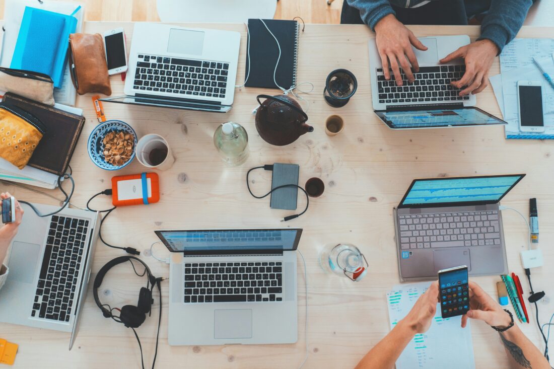 B2B tech messaging and positioning workspace with multiple laptops, mobile devices, notebooks, and team members collaborating around a shared table.